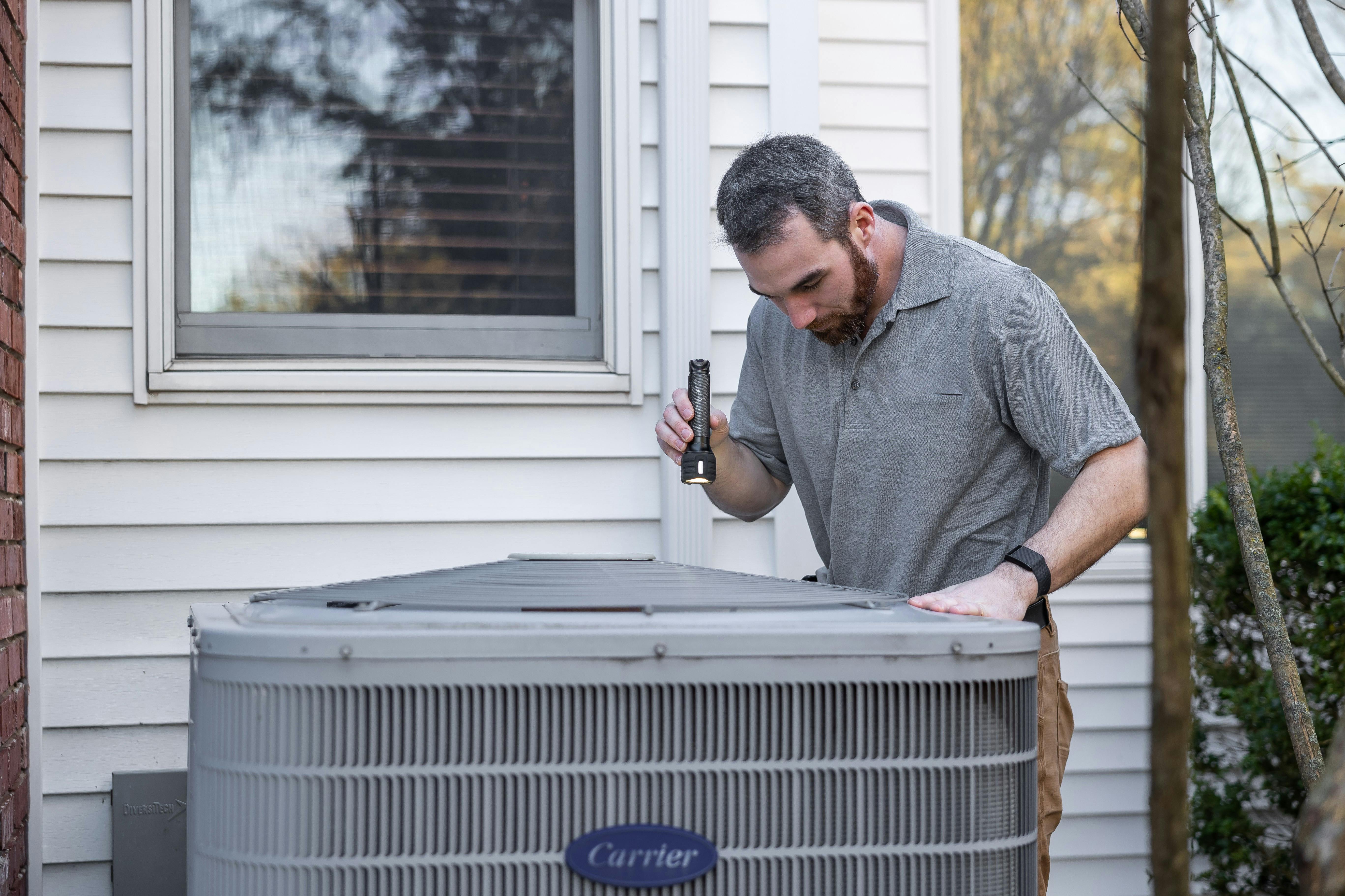 An HVAC technician inspecting an outdoor Carrier condenser unit at a residential home